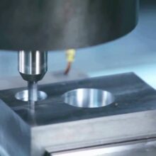 Marmon Keystone A close-up of a CNC milling machine cutting a circular hole in a metal bar, with another completed hole visible beside the cutting tool. The clean, industrial environment highlights precision metalwork for supplychain distributors.