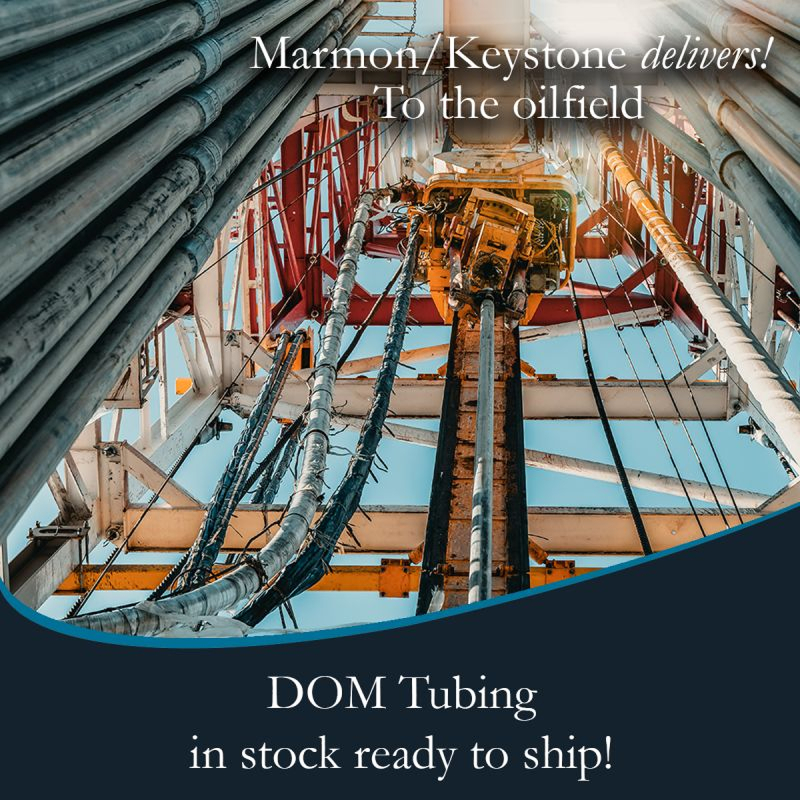 post-1-4 Marmon Keystone View looking up at steel pipes and equipment on an oil drilling rig, with text promoting Marmon/Keystone as your trusted metals distributor—with DOM tube and pipe in stock and ready to ship for oilfield supply chain needs.