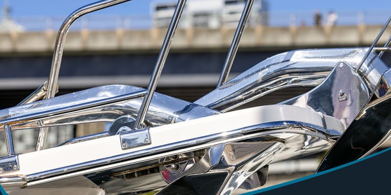 post-1-8 Marmon Keystone Close-up of polished stainless steel tubing on a boat railing with promotional text for Marmon/Keystone welded stainless tube and pipe, A269. In-stock metals, ready to ship from your trusted supply chain distributor. Bridge and sky in the background.